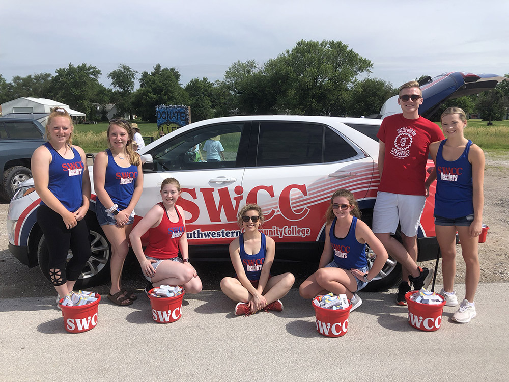 Spartan Dazzlers and coach posing in front of a SWCC vehicle.